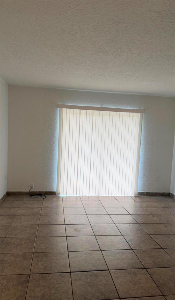 An empty room with beige tile flooring and vertical blinds covering a sliding glass door — 4344 NW 9th Avenue # 3f, Pompano Beach FL 33064, POMPANO BEACH, FL