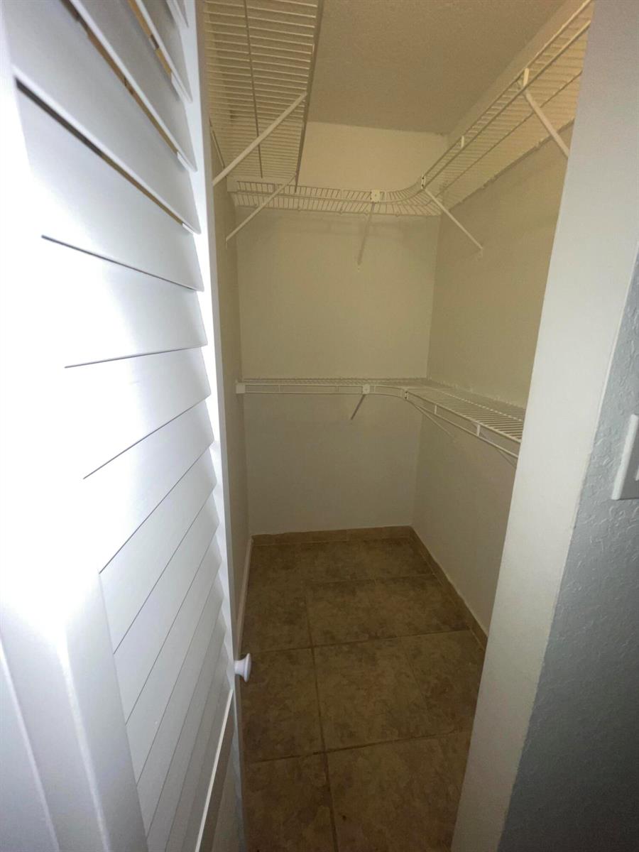 A walk-in closet features white wire shelving, beige tile flooring, and louvered double doors — 4344 NW 9th Avenue # 3f, Pompano Beach FL 33064, POMPANO BEACH, FL