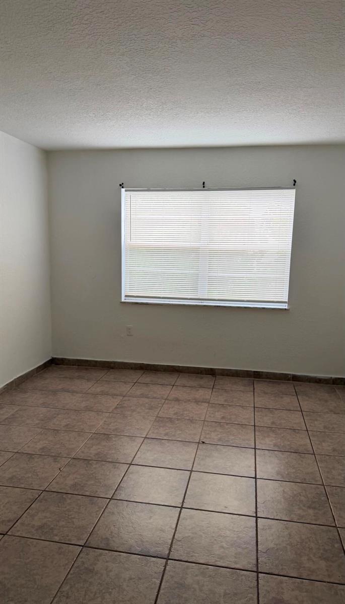 An empty room with beige tile flooring, white walls, and a window with closed blinds — 4344 NW 9th Avenue # 3f, Pompano Beach FL 33064, POMPANO BEACH, FL