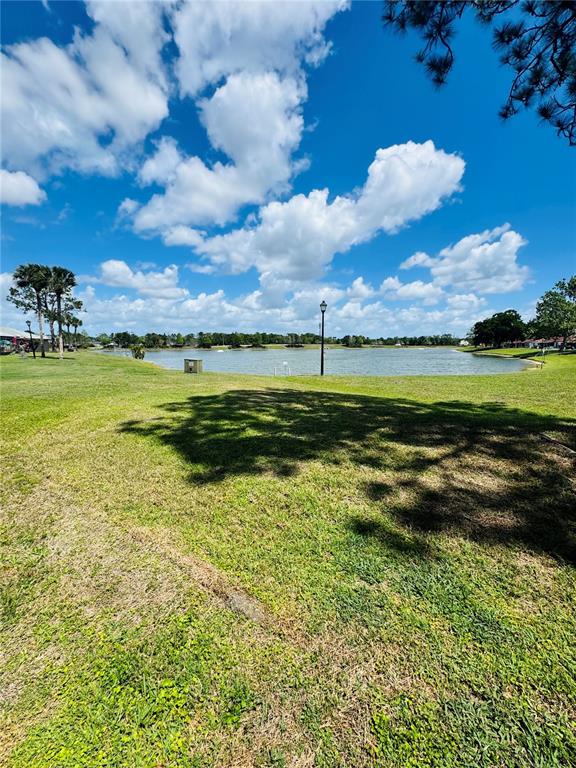 A grassy lawn leads to a lake under a blue sky with scattered clouds — 37 LAS BRISAS WAY UNIT 37, KISSIMMEE, FL