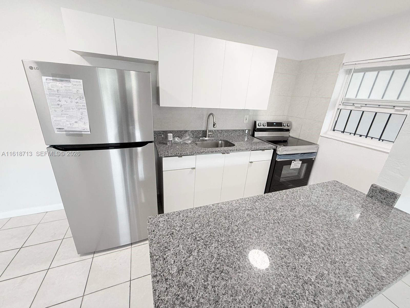A kitchen features white cabinets, granite countertops, stainless steel appliances, and light-colored tile flooring — 100 NE 78th St # 9, Miami FL 33138, MIAMI, FL