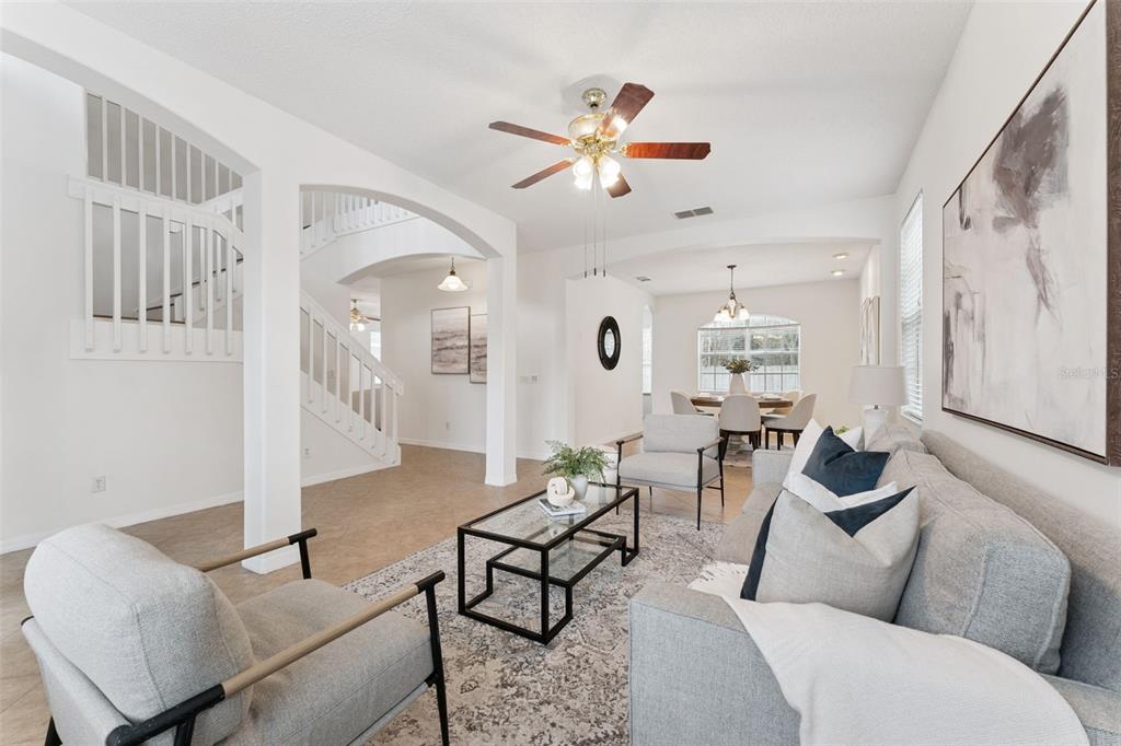 A bright living room features a staircase, light tile flooring, and neutral furniture — 2008 CHAPMAN OAKS DRIVE, OVIEDO, FL