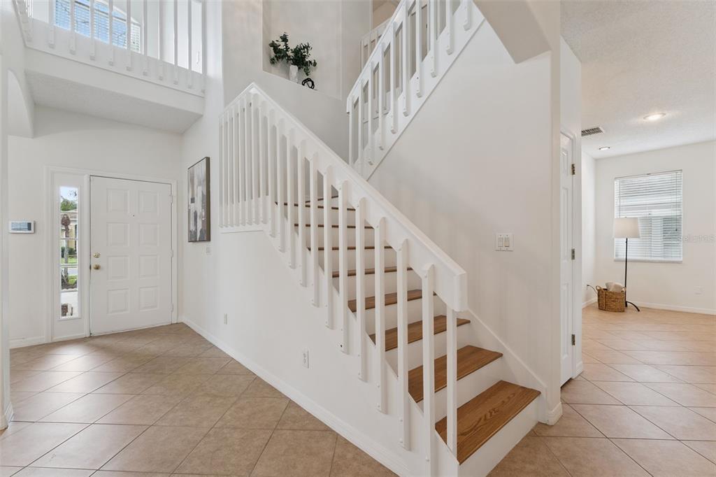 An entryway features a white staircase with wooden treads, tile flooring, and a front door — 2008 CHAPMAN OAKS DRIVE, OVIEDO, FL