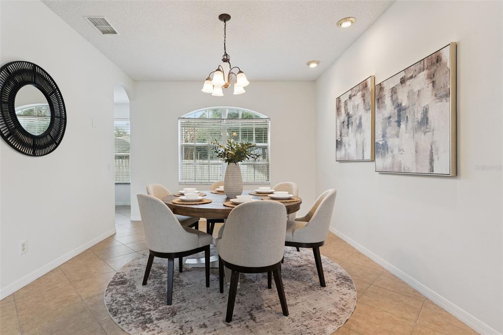 A dining room features a round wooden table, upholstered chairs, and two large abstract paintings — 2008 CHAPMAN OAKS DRIVE, OVIEDO, FL