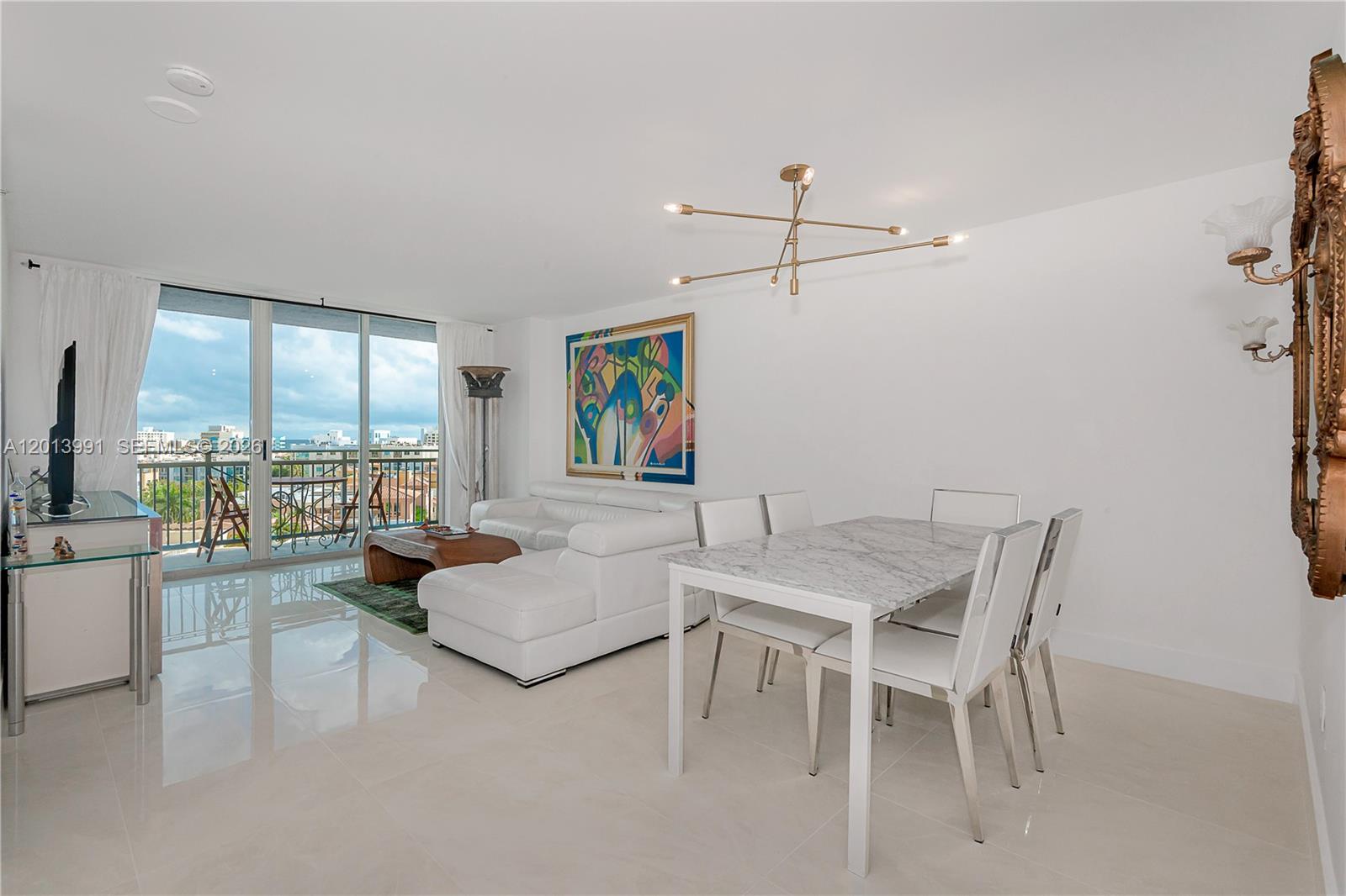 A bright living and dining area features white tile floors, modern furniture, and a balcony — 90 ALTON RD # 1007, Miami Beach FL 33139, MIAMI BEACH, FL