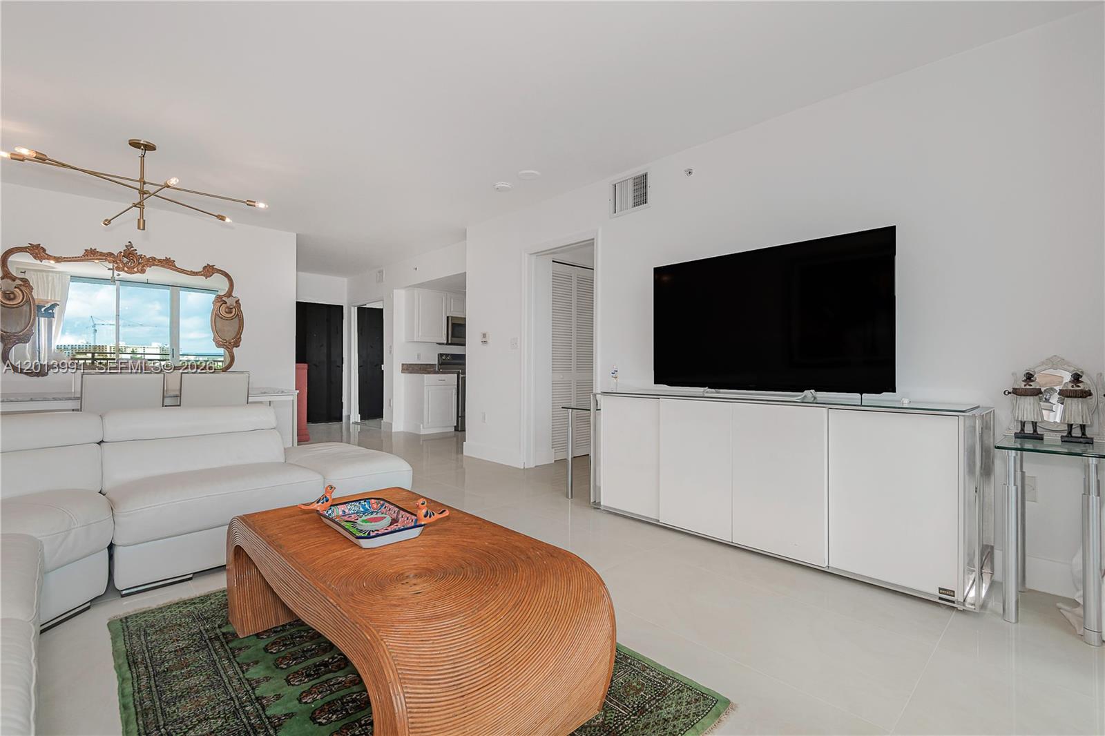 A living room features a white sectional sofa, a wooden coffee table, and a wall-mounted television — 90 ALTON RD # 1007, Miami Beach FL 33139, MIAMI BEACH, FL