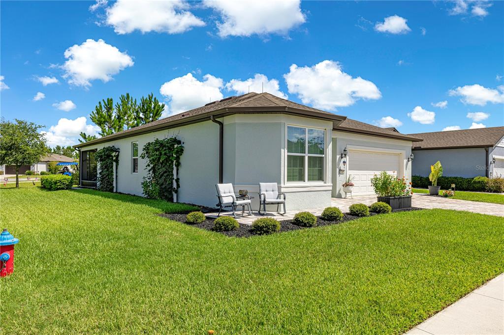 A single-story house with a paved patio, two chairs, and a garage under a blue sky — 9295 SW 60TH LANE ROAD, OCALA, FL
