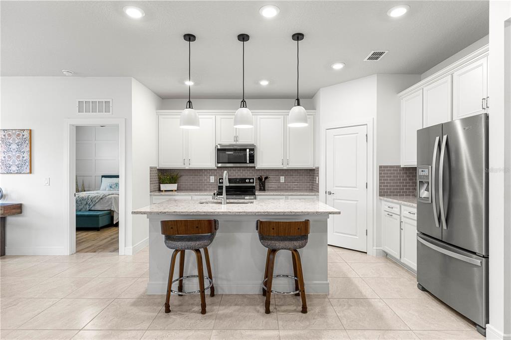 A modern kitchen features white cabinets, a granite island with two stools, and stainless appliances — 9295 SW 60TH LANE ROAD, OCALA, FL