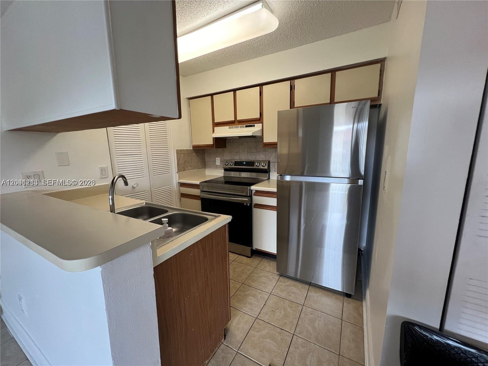A kitchen features stainless steel appliances, light-colored cabinets, tile flooring, and a sink peninsula — 1227 SW 46th Ave # 304, Pompano Beach FL 33069, POMPANO BEACH, FL