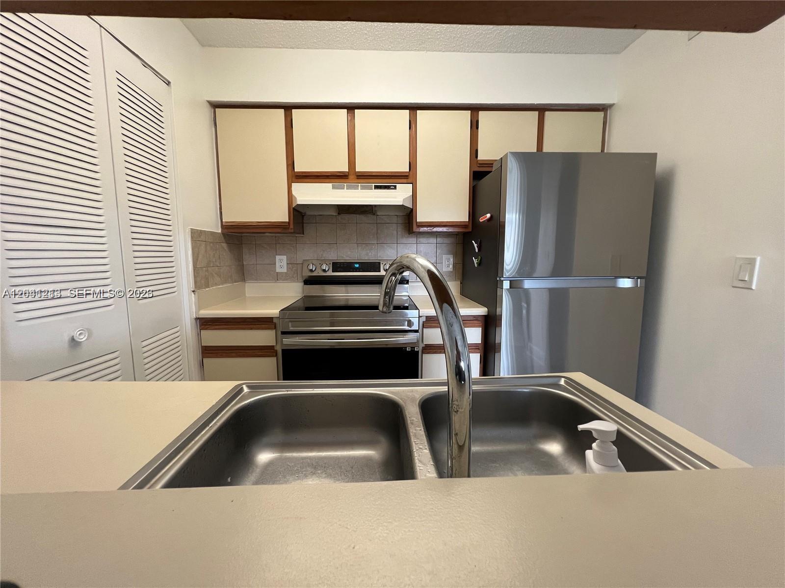 A kitchen features a double-basin sink, stainless steel appliances, and light-colored cabinets with wood trim — 1227 SW 46th Ave # 304, Pompano Beach FL 33069, POMPANO BEACH, FL