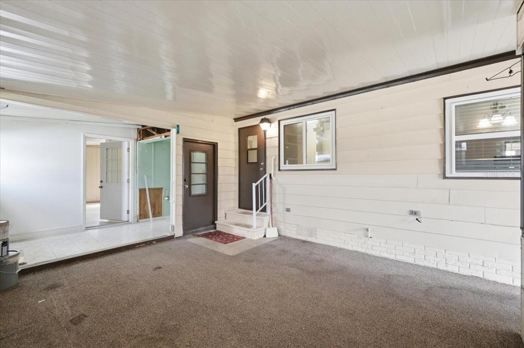 A covered carport features a brown door, white siding, and an adjacent open-air room — 1603 FOXWAY DRIVE, LAKELAND, FL