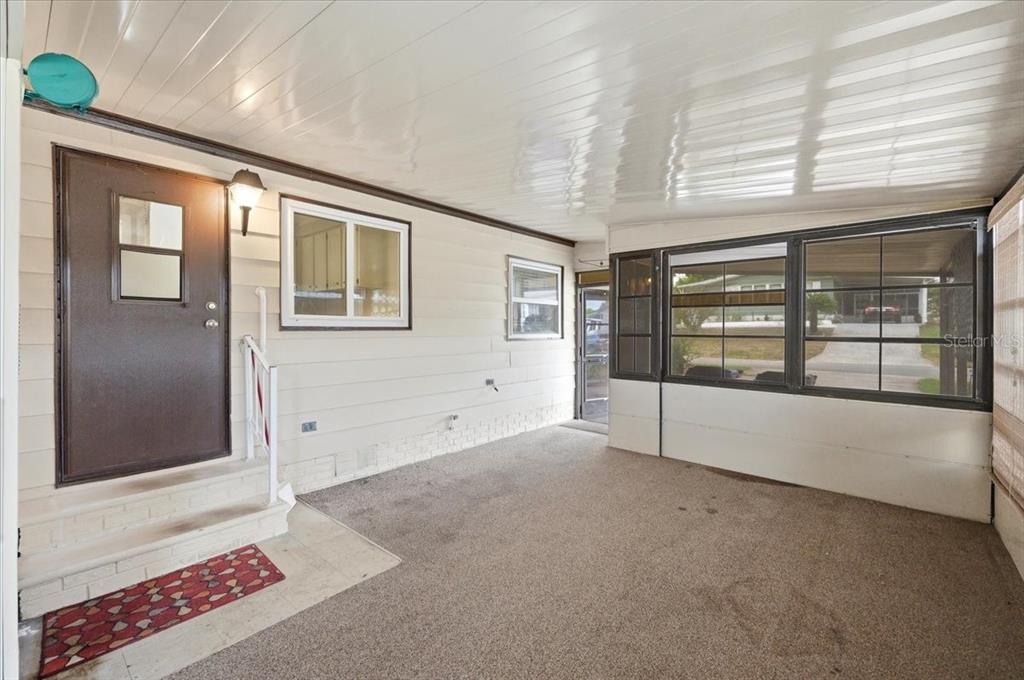 A covered outdoor patio with a brown door, large windows, and a textured concrete floor — 1603 FOXWAY DRIVE, LAKELAND, FL