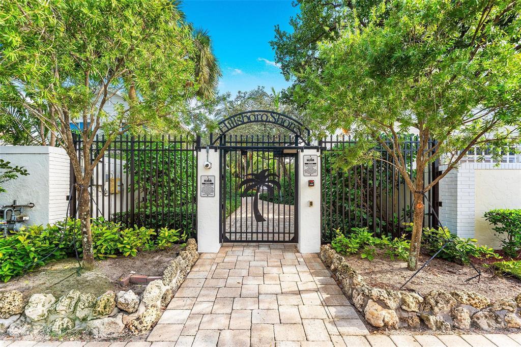 A gated entrance with a stone walkway leads to a path framed by lush green trees — 3213 Dover Road, Pompano Beach FL 33062, POMPANO BEACH, FL