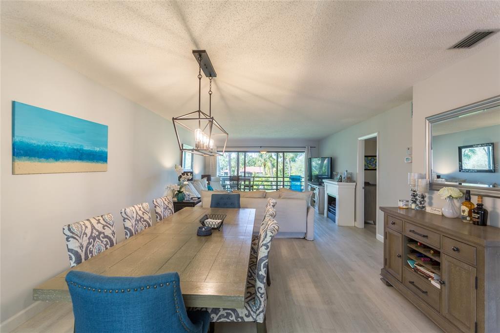 A dining area with a wooden table and patterned chairs leads into a living room — 3500 EL CONQUISTADOR PARKWAY UNIT 268, BRADENTON, FL