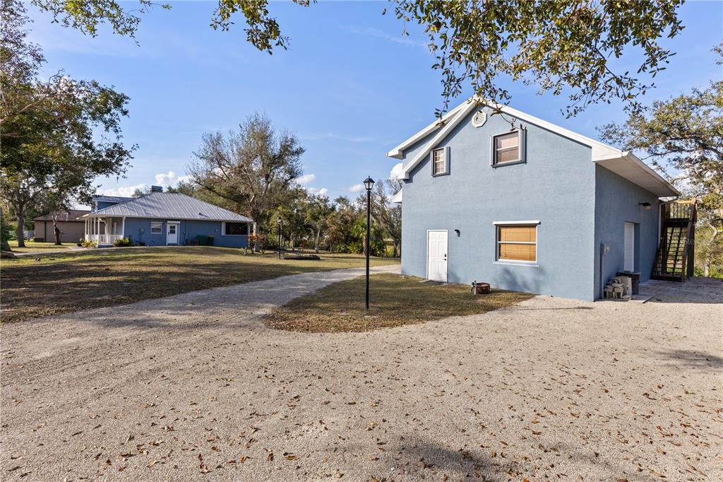 A blue two-story building stands next to a gravel driveway with a house in the background — 27350 SAN CARLOS DRIVE, PUNTA GORDA, FL