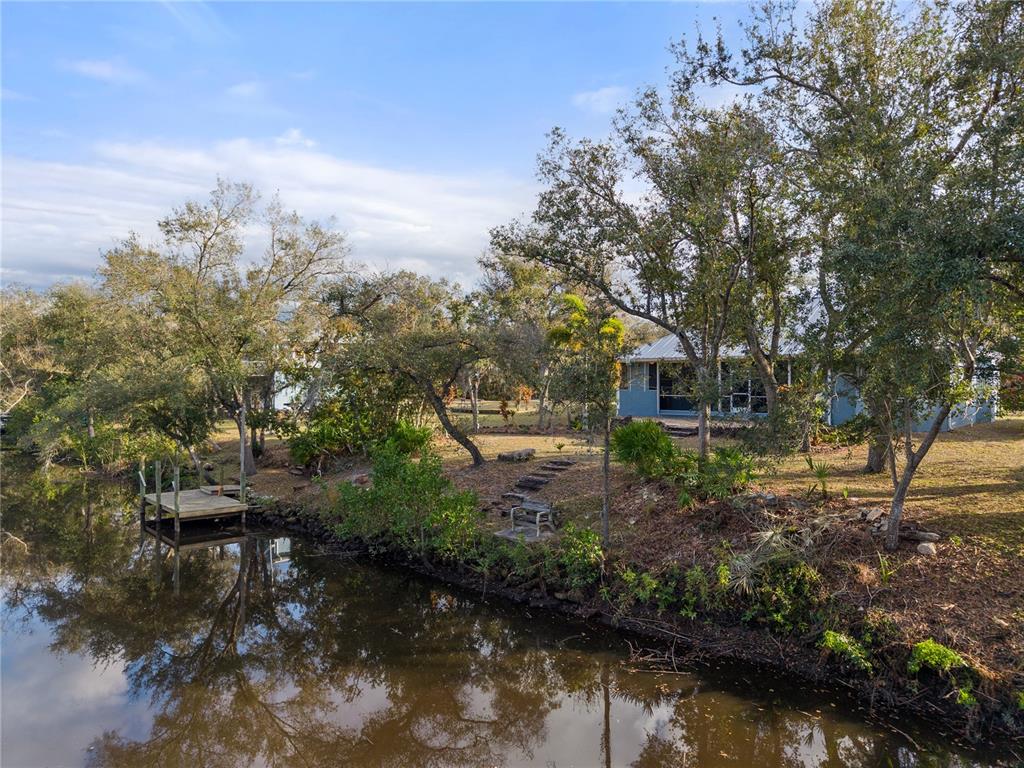 An exterior view of a waterfront house with a wooden dock and mature trees — 27350 SAN CARLOS DRIVE, PUNTA GORDA, FL