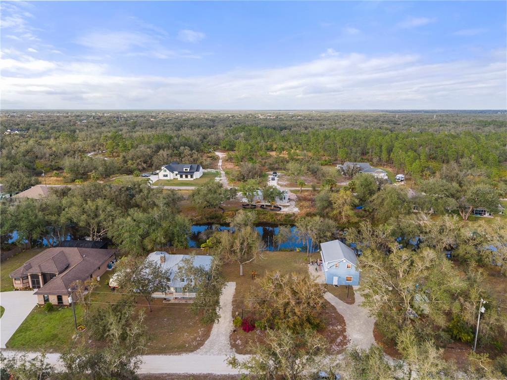 An aerial view shows several houses situated near a small pond surrounded by wooded areas — 27350 SAN CARLOS DRIVE, PUNTA GORDA, FL
