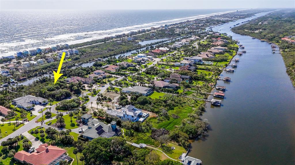 An aerial view shows a coastal neighborhood with houses, a river, and a yellow arrow — 153 ISLAND ESTATES PARKWAY, PALM COAST, FL