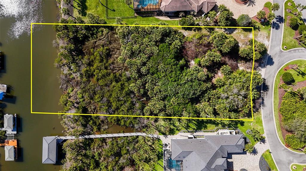 An aerial view shows a rectangular, tree-covered vacant lot situated between a waterway and a road — 153 ISLAND ESTATES PARKWAY, PALM COAST, FL
