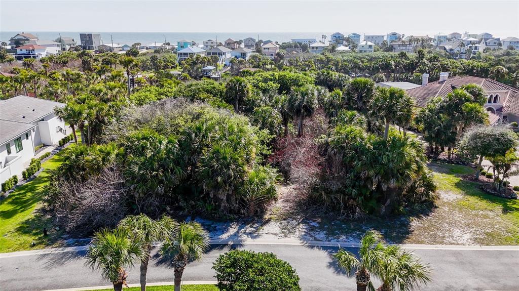 An aerial view shows a vacant, wooded residential lot situated between two houses near the ocean — 153 ISLAND ESTATES PARKWAY, PALM COAST, FL