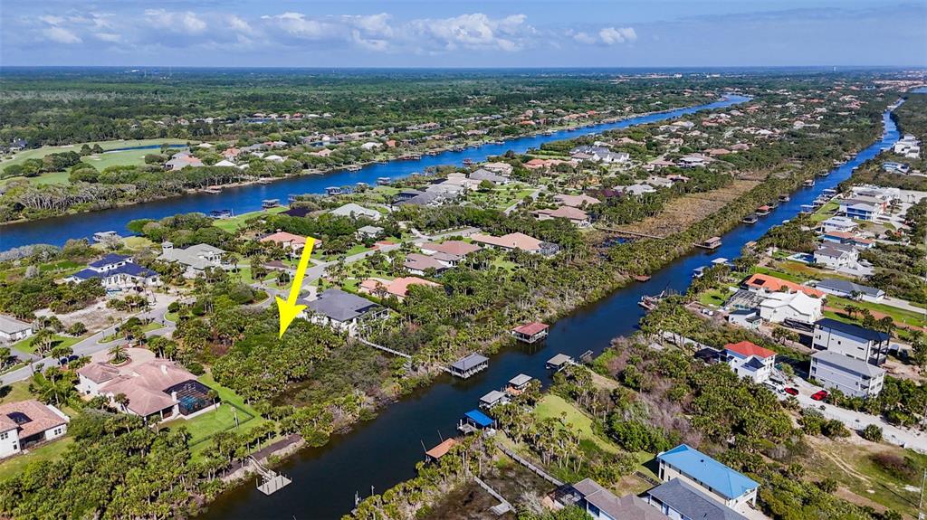 An aerial view shows a residential neighborhood with a yellow arrow pointing toward a wooded lot — 153 ISLAND ESTATES PARKWAY, PALM COAST, FL