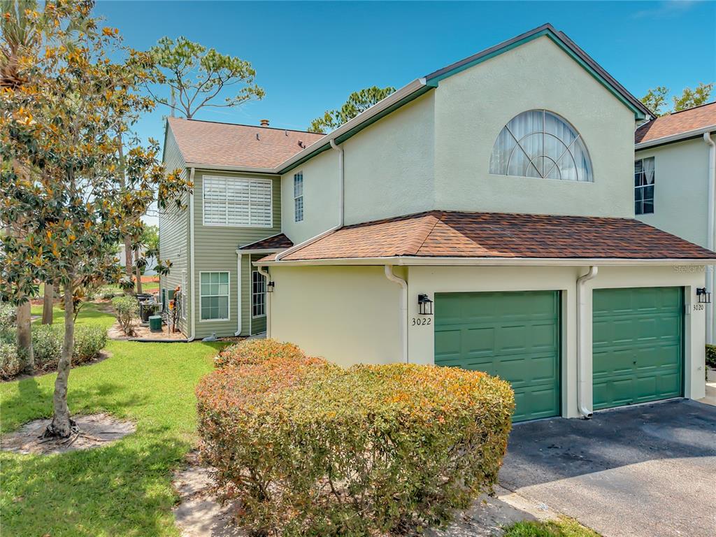 A two-story townhouse with green garage doors, light-colored siding, and a landscaped front yard — 3022 COTTAGE GROVE COURT UNIT 1807, ORLANDO, FL