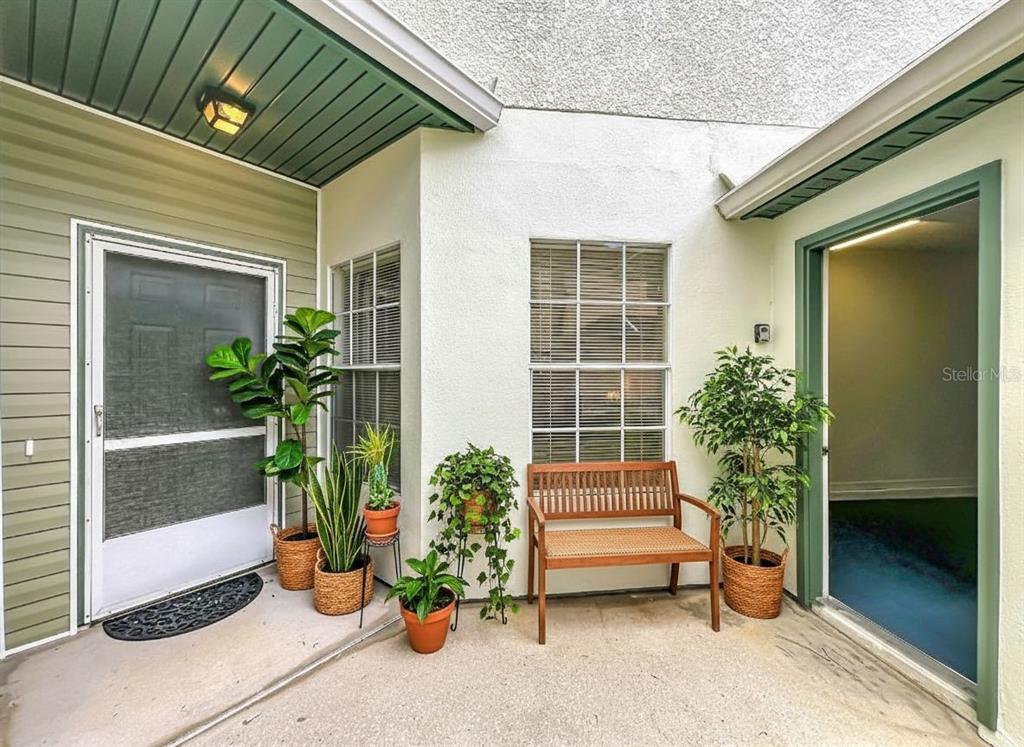 A patio area features a wooden bench, potted plants, and two doorways with green trim — 3022 COTTAGE GROVE COURT UNIT 1807, ORLANDO, FL