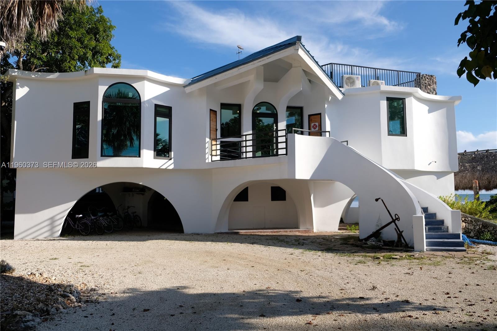 A white, elevated house with arched ground-level openings and an exterior staircase leading to a balcony — 1557 Long Beach Dr, FL 33043, FL