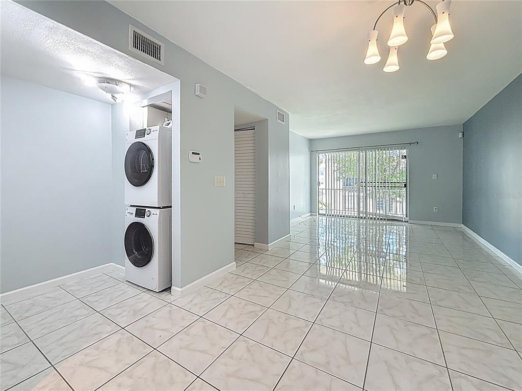 A room with white tiled floors, a stacked washer and dryer, and a sliding glass door — 2625 STATE ROAD 590 UNIT 724, CLEARWATER, FL