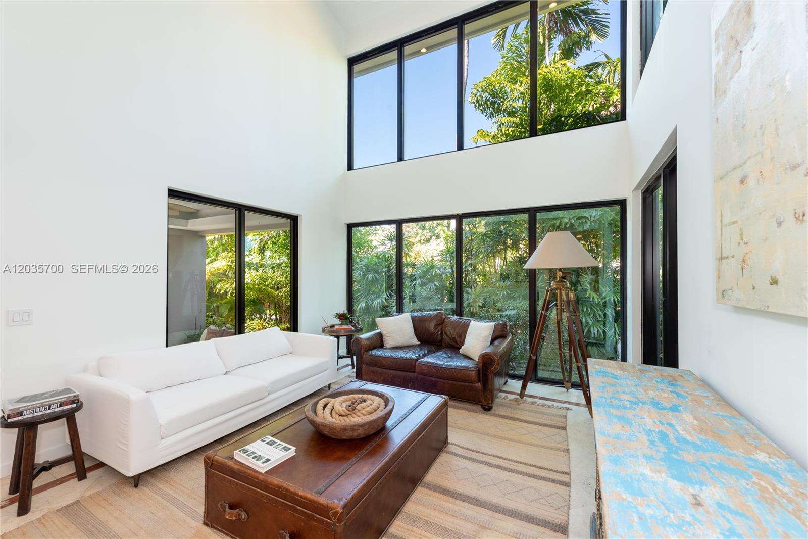 A living room features a white sofa, leather loveseat, trunk coffee table, and floor-to-ceiling windows — 650 Curtiswood Dr, Key Biscayne FL 33149, KEY BISCAYNE, FL