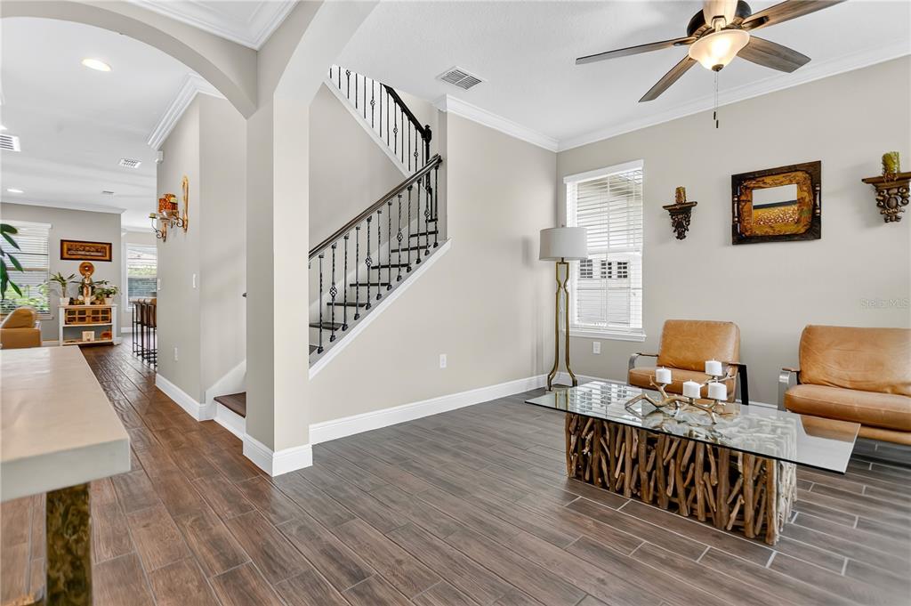 A living room features wood-look tile flooring, a staircase with iron railings, and leather chairs — 10007 LITTLE ALCOVE LOOP, WINTER GARDEN, FL