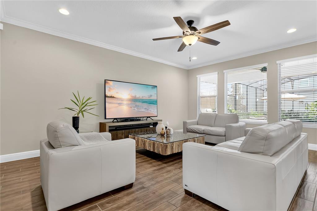 A living room features white leather furniture, a glass-topped coffee table, and wood-look tile flooring — 10007 LITTLE ALCOVE LOOP, WINTER GARDEN, FL