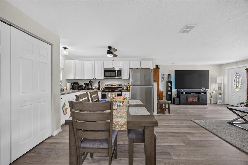 An open-concept kitchen and living area featuring white cabinets, stainless steel appliances, and wood-look flooring — 1608 YANCY STREET, PORT CHARLOTTE, FL