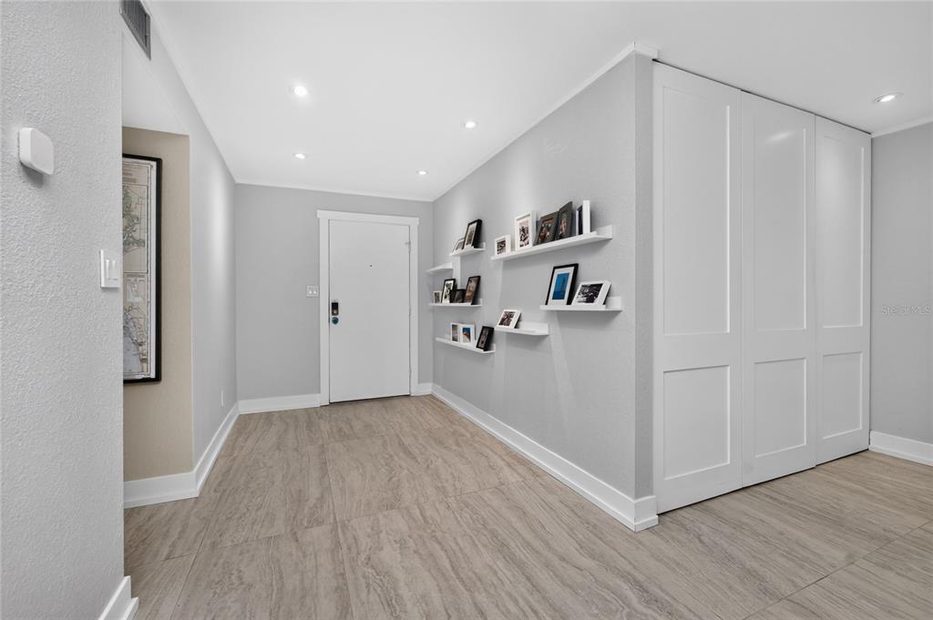 A light-colored entryway features wood-look tile flooring, white walls, floating shelves, and a closet — 25188 MARION AVENUE UNIT D101, PUNTA GORDA, FL