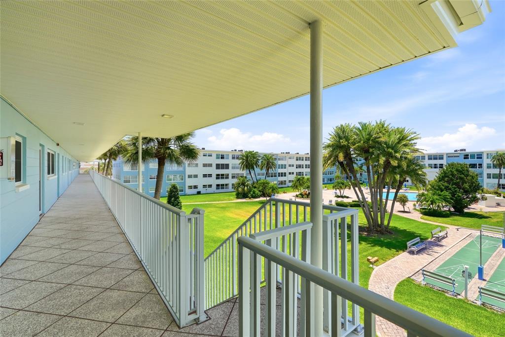 An outdoor walkway overlooks a courtyard with a swimming pool, palm trees, and a court — 6201 2ND STREET E UNIT 106, ST PETE BEACH, FL