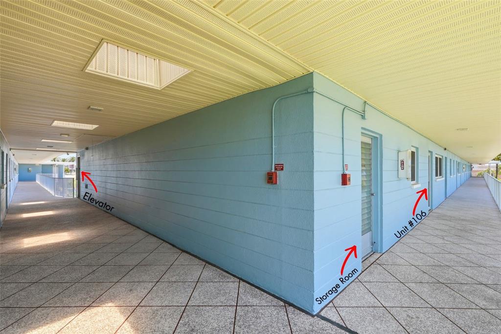 An outdoor apartment building walkway with blue walls, tiled floors, and labeled unit entrances — 6201 2ND STREET E UNIT 106, ST PETE BEACH, FL