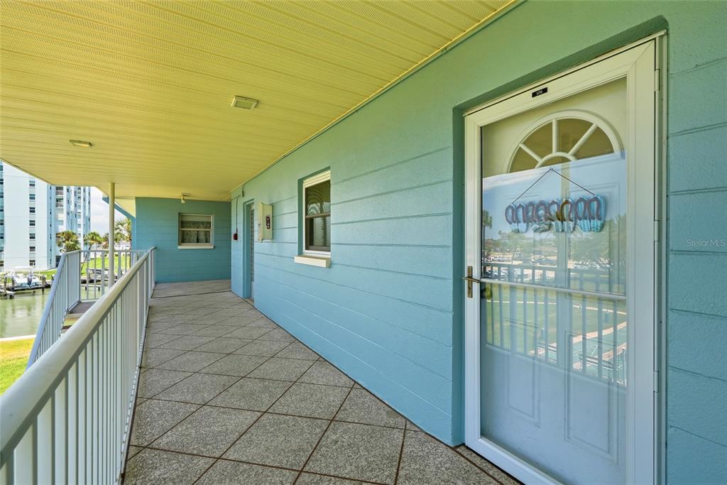 A light blue exterior walkway with a tiled floor and a white door — 6201 2ND STREET E UNIT 106, ST PETE BEACH, FL