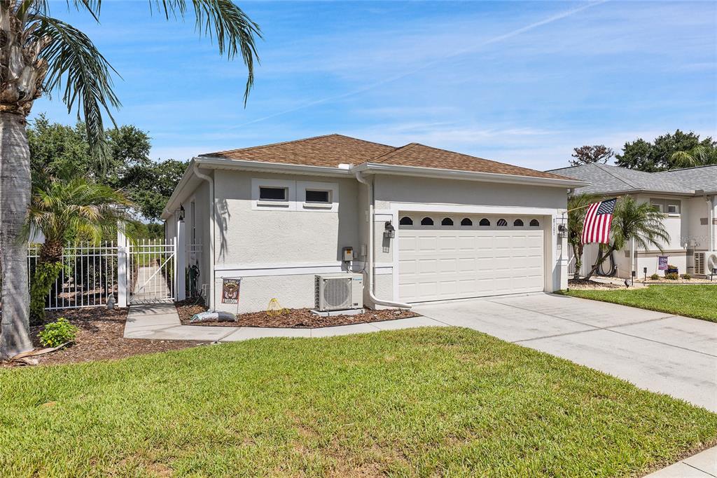 A beige house exterior features a two-car garage, a concrete driveway, and a side gate — 8107 PONKAN ROAD, LAND O LAKES, FL