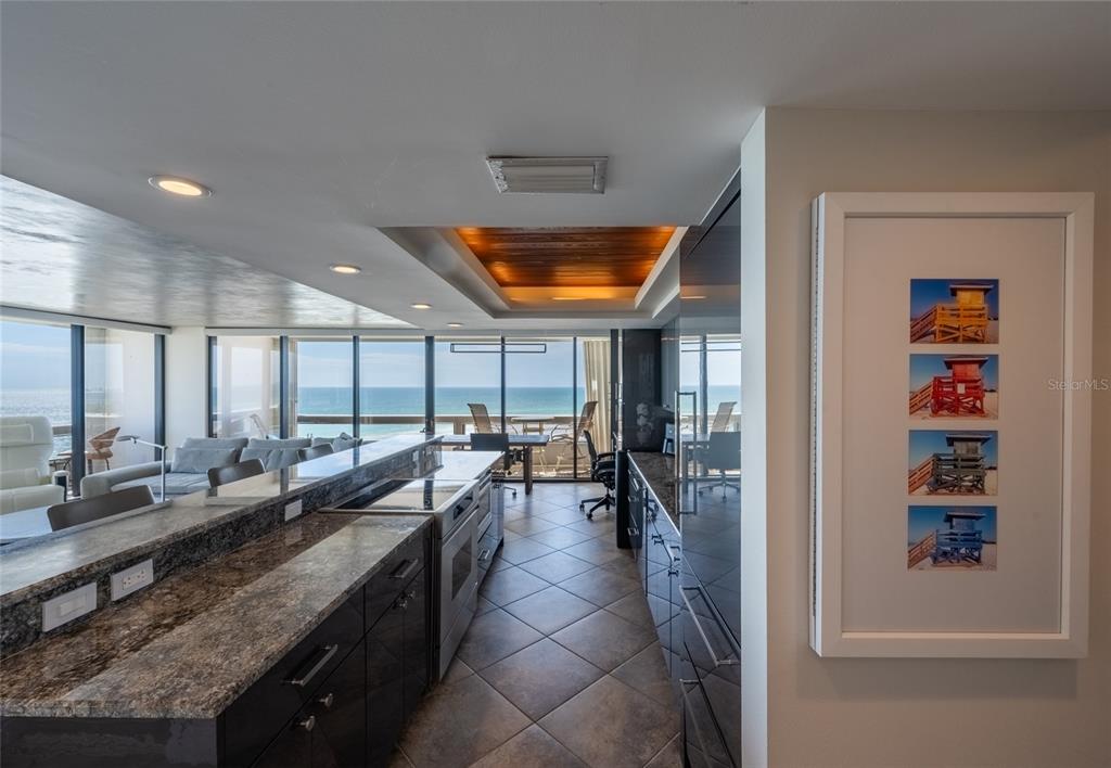 A modern kitchen with dark cabinetry and granite countertops overlooks a balcony and the ocean — 5400 OCEAN BOULEVARD UNIT 10-02, SARASOTA, FL