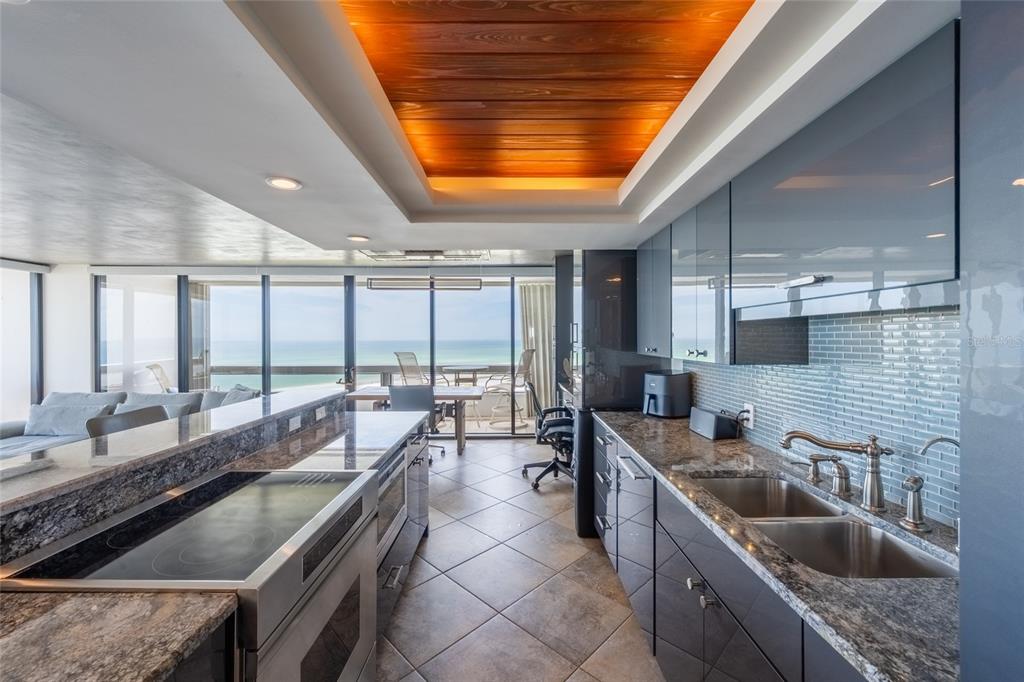 A modern kitchen with dark cabinetry, granite countertops, and a wood-paneled ceiling overlooking the ocean — 5400 OCEAN BOULEVARD UNIT 10-02, SARASOTA, FL