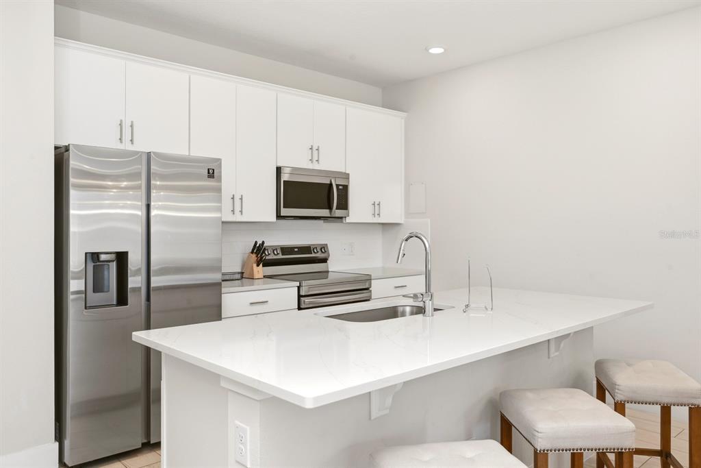 A modern kitchen features white cabinets, stainless steel appliances, and a white quartz island countertop — 7909 DRAW STREET, REUNION, FL
