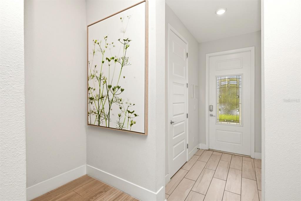 An entryway features light wood-look tile flooring, a white door with glass, and wall art — 7909 DRAW STREET, REUNION, FL