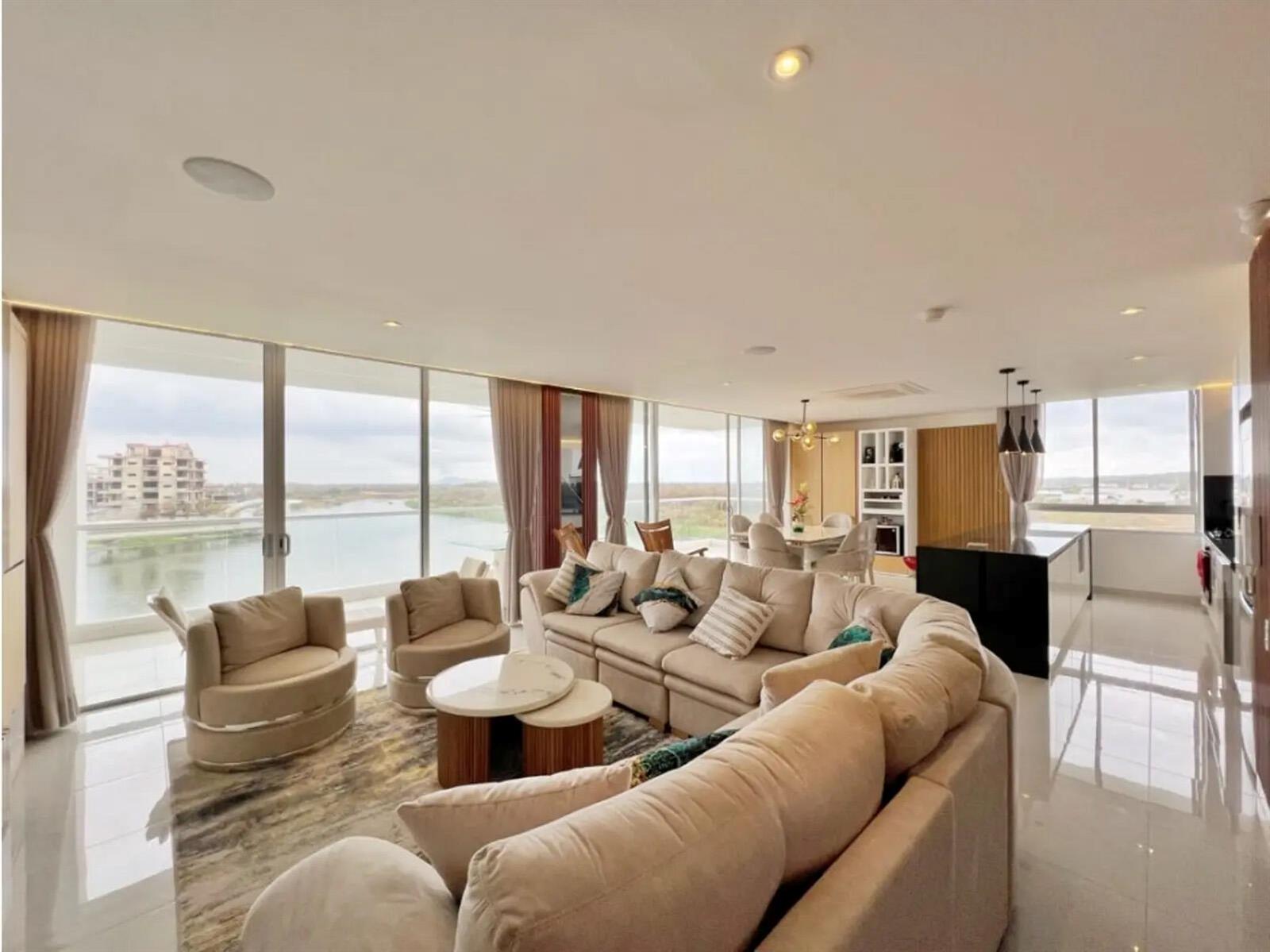 A modern open-concept living room with a large sectional sofa, dining area, and waterfront views — Km 8 Via Al Mar, FL