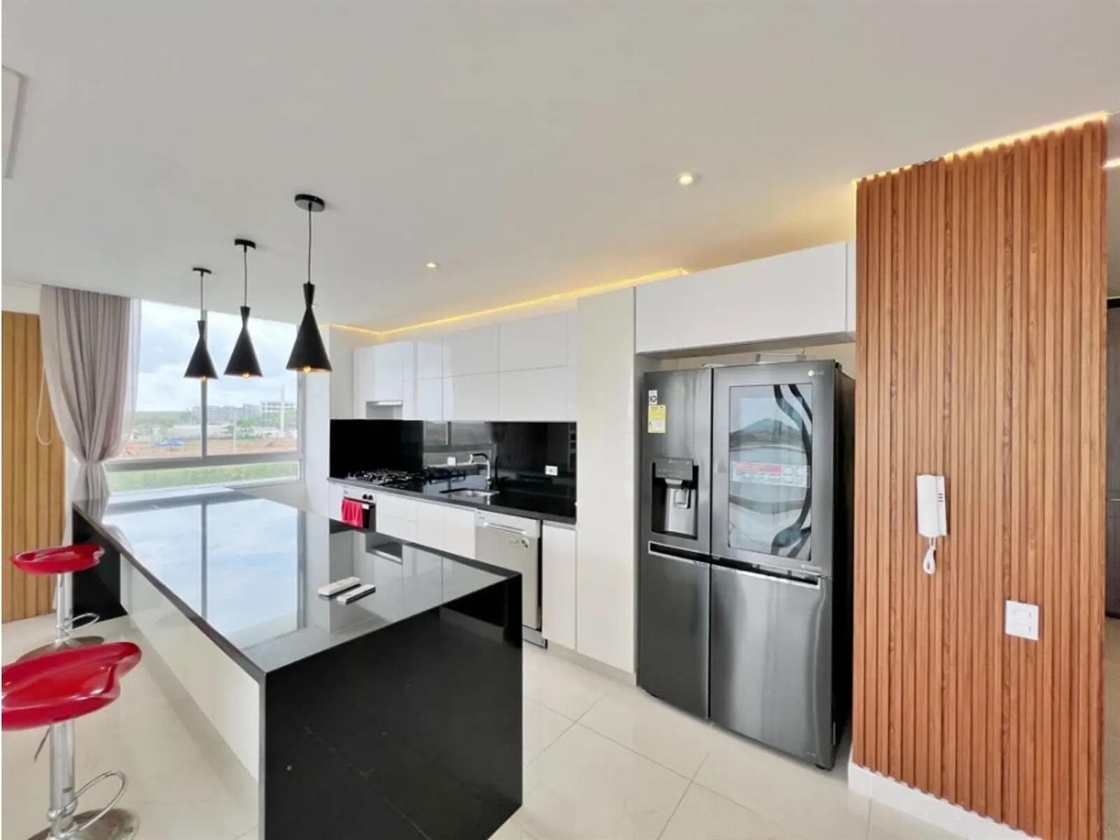 A modern kitchen features a black island, white cabinetry, stainless steel appliances, and wood-slatted walls — Km 8 Via Al Mar, FL