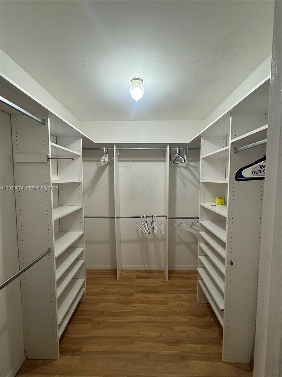 A walk-in closet features white shelving units, hanging rods, and light wood-look flooring — 6731 Cypress Rd # 410, Plantation FL 33317, PLANTATION, FL