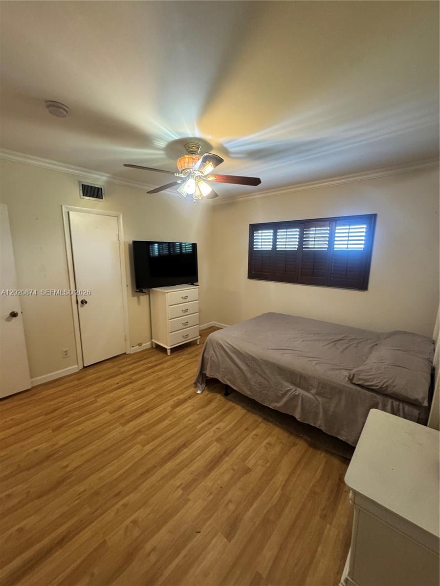 A bedroom features light wood-look flooring, a ceiling fan, a bed, and a white dresser — 6731 Cypress Rd # 410, Plantation FL 33317, PLANTATION, FL