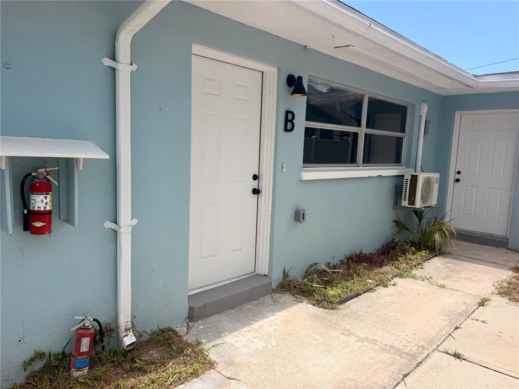 The exterior of a light blue building features two white doors, a window, and fire extinguishers — 13388 1ST STREET E UNIT B, MADEIRA BEACH, FL