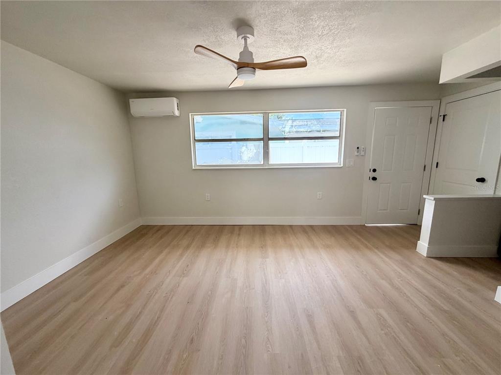 A room with light wood-look flooring, a ceiling fan, a window, and a wall-mounted AC unit — 13388 1ST STREET E UNIT B, MADEIRA BEACH, FL