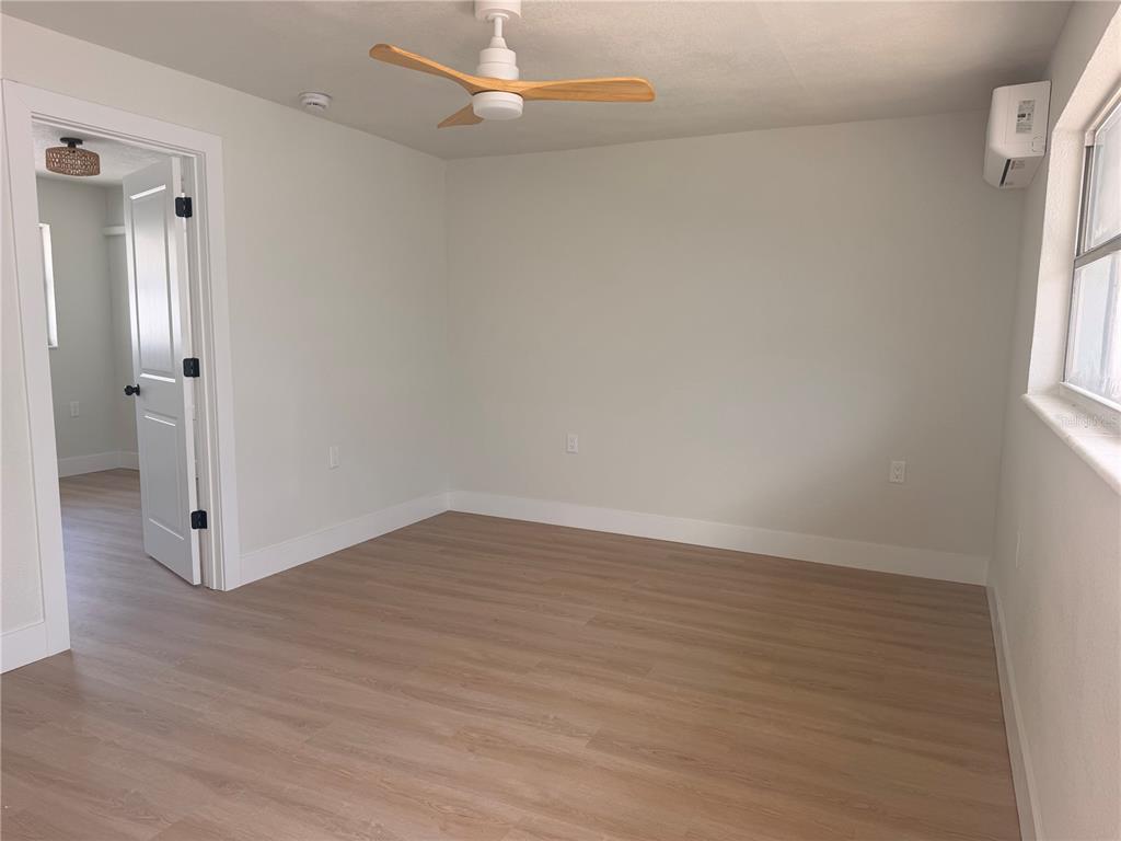A bedroom with light-colored walls, wood-look flooring, a ceiling fan, and a mini-split unit — 13388 1ST STREET E UNIT B, MADEIRA BEACH, FL