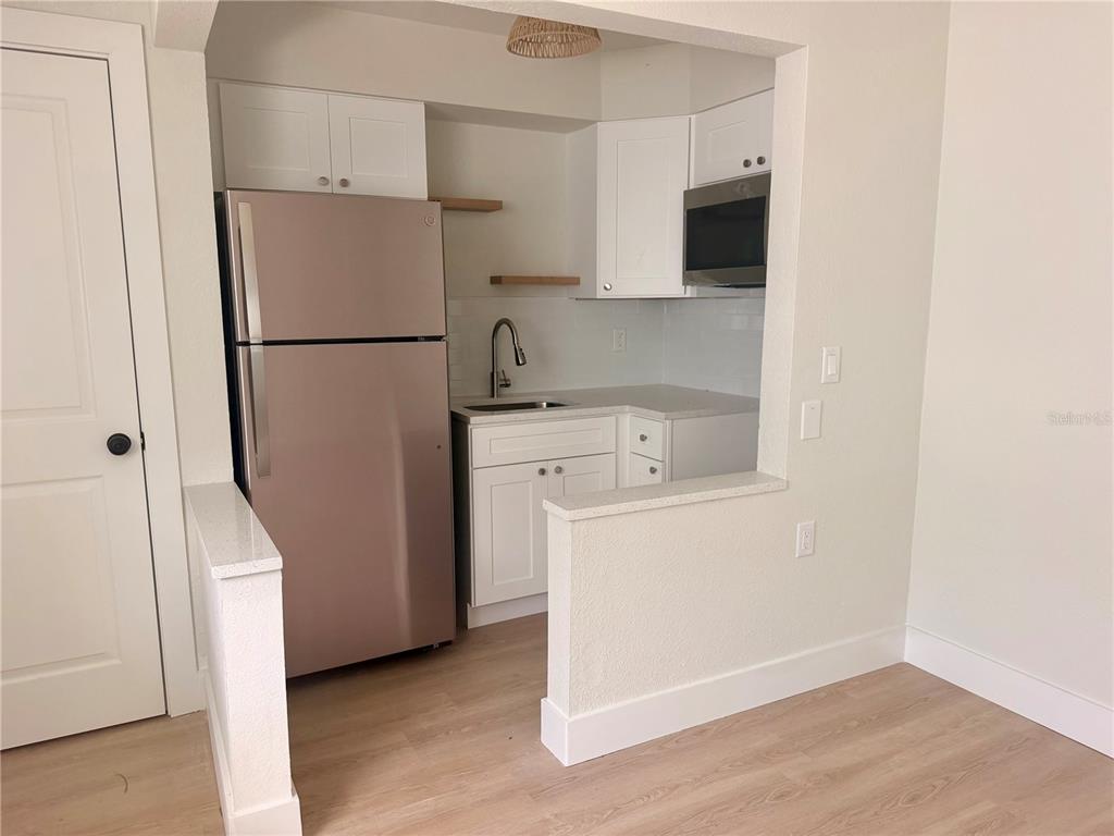 A small kitchen features white cabinets, stainless steel appliances, and light wood-look flooring — 13388 1ST STREET E UNIT B, MADEIRA BEACH, FL